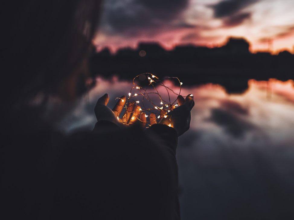 eft tapping blog person holding string of lights over water at sunset